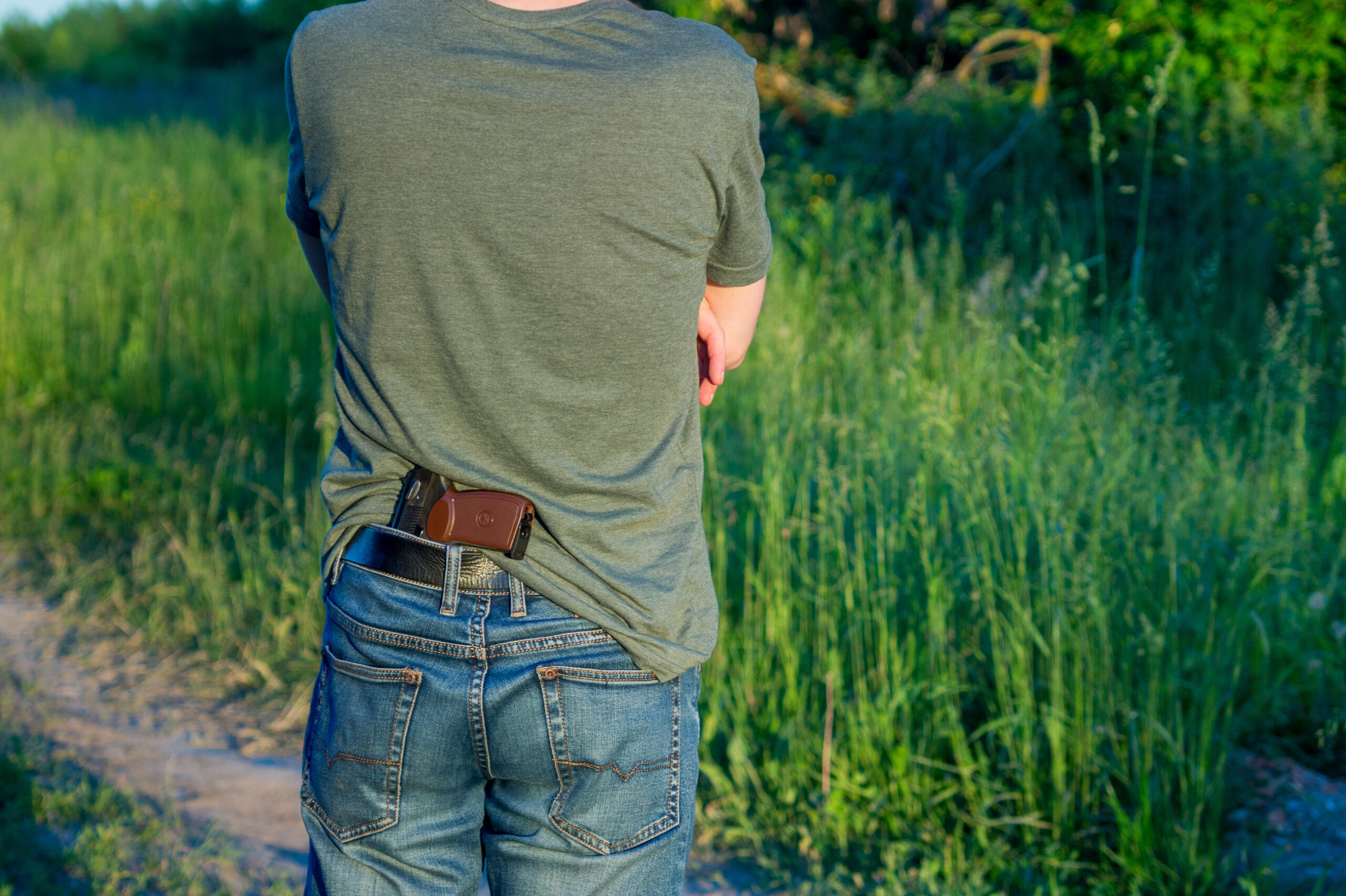 Man,Hides,A,Weapon,In,Jeans,,A,Field,With,Grass,